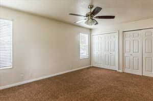 Unfurnished bedroom featuring carpet floors, two closets, baseboards, a textured ceiling, and a ceiling fan