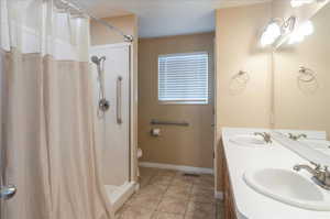 Bathroom with baseboards, curtained shower, tile patterned flooring, toilet, and double vanity
