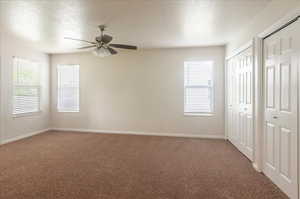 Unfurnished bedroom featuring multiple closets, light colored carpet, a textured ceiling, and baseboards