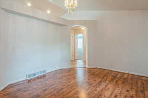 Unfurnished room with arched walkways, wood finished floors, baseboards, and a chandelier