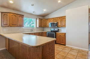 Kitchen with stainless steel appliances, a sink, brown cabinetry, a peninsula, and light countertops