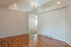 Unfurnished room featuring arched walkways, a chandelier, baseboards, wood finished floors, and vaulted ceiling