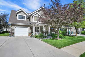 View of front facade with a front lawn, concrete driveway, a porch, a shingled roof, and stone siding