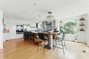 Kitchen featuring appliances with stainless steel finishes, a breakfast bar, backsplash, light wood-type flooring, and decorative light fixtures