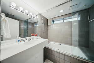 Full bath with tiled shower / bath combo, vanity, and tile walls