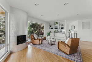 Living room with a fireplace with raised hearth, wood finished floors, and recessed lighting