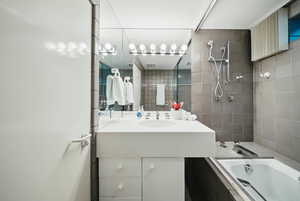 Bathroom featuring tiled shower / bath, vanity, and tile walls
