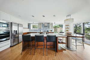 Kitchen featuring appliances with stainless steel finishes, wall chimney exhaust hood, white cabinetry, tasteful backsplash, and a breakfast bar