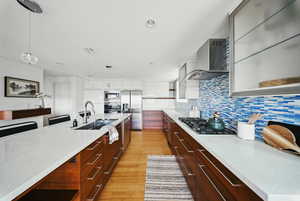Kitchen featuring wall chimney exhaust hood, modern cabinets, stainless steel appliances, a sink, and open shelves