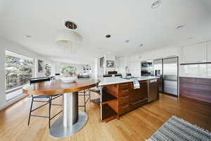 Kitchen featuring appliances with stainless steel finishes, a sink, light countertops, light wood-type flooring, and hanging light fixtures