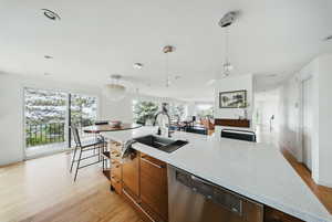 Kitchen with dishwasher, a sink, modern cabinets, light wood-style floors, and hanging light fixtures