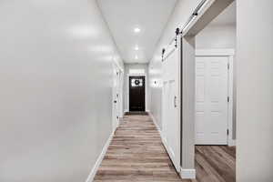 Corridor with light wood-style flooring, a barn door, recessed lighting, and baseboards
