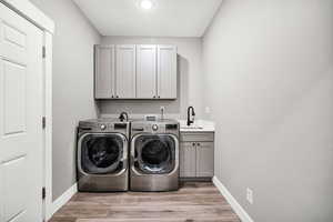 Washroom featuring cabinet space, washing machine and dryer, baseboards, and light wood-type flooring