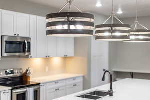 Kitchen with appliances with stainless steel finishes, white cabinets, a sink, light countertops, and recessed lighting