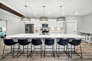 Kitchen with stainless steel appliances, a large island, recessed lighting, light wood finished floors, and white cabinetry