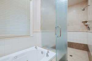 Full bathroom with a shower stall, a tub with jets, and tile walls