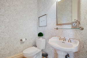 Half bathroom with toilet, wallpapered walls, and a sink