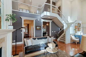 Living room with wood-type flooring, stairs, a towering ceiling, baseboards, and a tiled fireplace