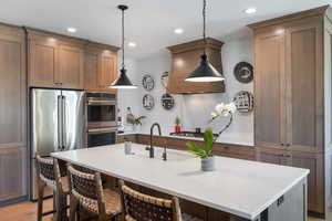 Kitchen with stainless steel appliances, a sink, a breakfast bar, pendant lighting, and light countertops