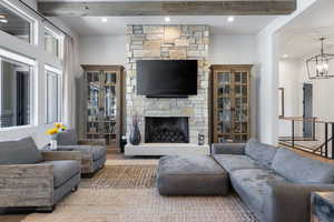 Living room with beamed ceiling, a chandelier, and a stone fireplace