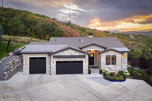 Contemporary house with a garage, stone siding, concrete driveway, a chimney, and roof with shingles