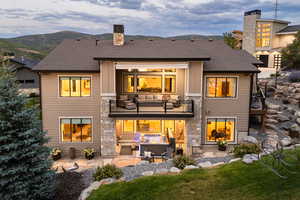 Back of house with a chimney, a balcony, a patio area, roof with shingles, and a lawn
