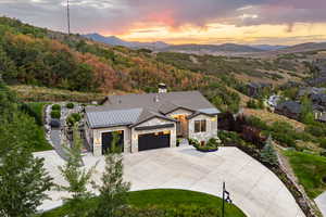Modern inspired farmhouse with driveway, an attached garage, stone siding, a chimney, and a metal roof