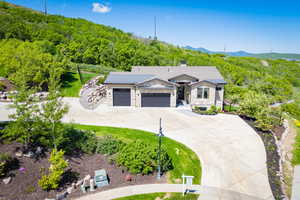 View of front of home with driveway, a garage, stone siding, a mountain view, and a chimney