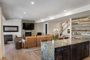 Living room featuring a large fireplace, light wood finished floors, stairway, and recessed lighting