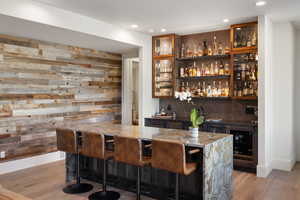 Indoor wet bar featuring beverage cooler, wood walls, light wood-type flooring, recessed lighting, and decorative backsplash