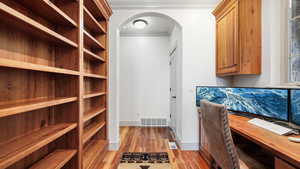 Office area featuring ornamental molding, arched walkways, light wood-style flooring, and baseboards