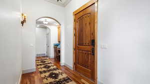 Entryway with crown molding, arched walkways, light wood-type flooring, and baseboards