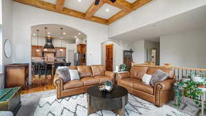 Living room featuring arched walkways, a high ceiling, coffered ceiling, beam ceiling, and light wood-type flooring