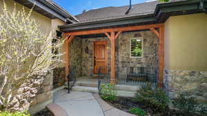 View of exterior entry featuring stone siding, stucco siding, covered porch, and a shingled roof