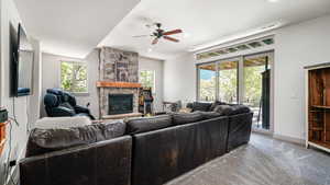 Living room featuring a stone fireplace, a ceiling fan, light colored carpet, baseboards, and recessed lighting