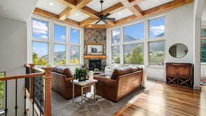 Living room featuring wood finished floors, a high ceiling, a ceiling fan, a fireplace, and beamed ceiling