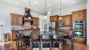 Kitchen with stainless steel appliances, a sink, backsplash, a center island with sink, and brown cabinetry