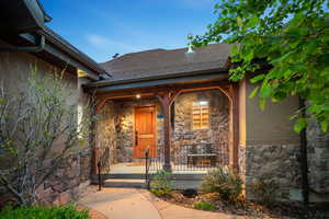 Entrance to property with stone siding, stucco siding, covered porch, and roof with shingles