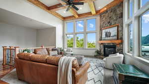 Living room featuring healthy amount of natural light, a fireplace, a ceiling fan, beam ceiling, and a towering ceiling