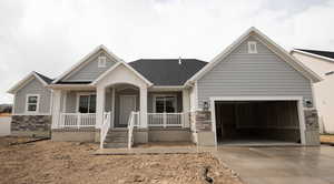 View of front of property with stone siding, an attached garage, a porch, and driveway