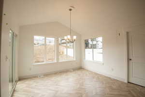 Unfurnished dining area with a chandelier, healthy amount of natural light, vaulted ceiling, and baseboards