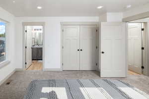 Unfurnished bedroom featuring light colored carpet, baseboards, recessed lighting, a closet, and ensuite bath