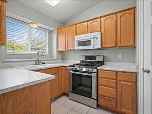 Kitchen featuring stainless steel gas range, white microwave, light tile patterned flooring, light countertops, and a sink