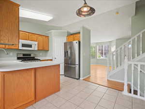 Kitchen with appliances with stainless steel finishes, light tile patterned flooring, light countertops, a peninsula, and a sink