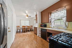 Kitchen featuring black appliances, light countertops, ceiling fan, light wood-style floors, and a sink