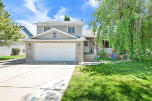 Split level home with brick siding, concrete driveway, a front lawn, and an attached garage