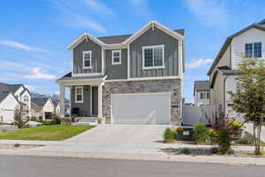 View of front of home with board and batten siding, an attached garage, stone siding, and driveway