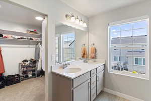 Full bath featuring a spacious closet, double vanity, and baseboards