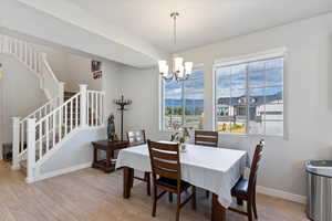 Dining area with stairs, light wood finished floors, a chandelier, and baseboards
