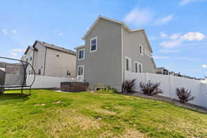 Rear view of property with a hot tub, a trampoline, and stucco siding